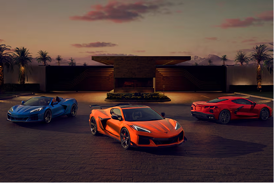 Corvette Stingray, Z06 und E-Ray stehen Heck an Heck in Fächerformation vor einem tropischen Sonnenuntergang.