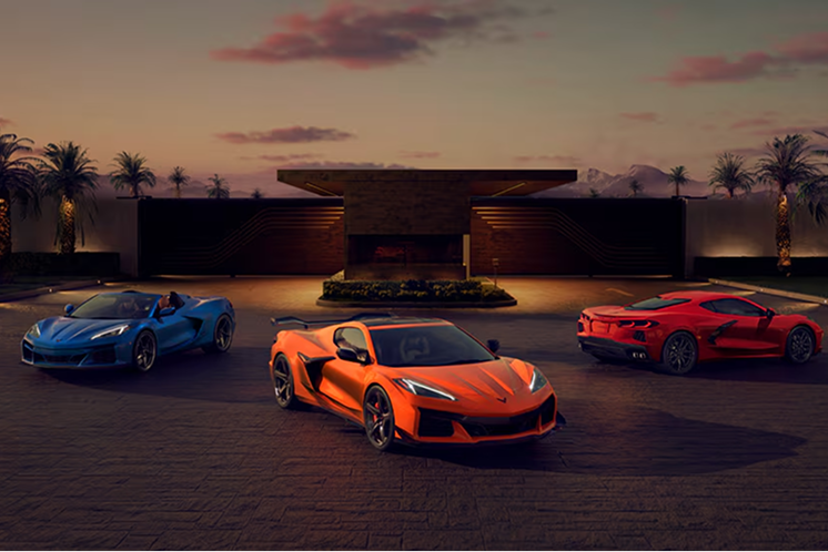 Corvette Stingray, Corvette Z06 und Corvette E-Ray, Heck an Heck fächerförmig geparkt, vor einem tropischen Sonnenuntergang.