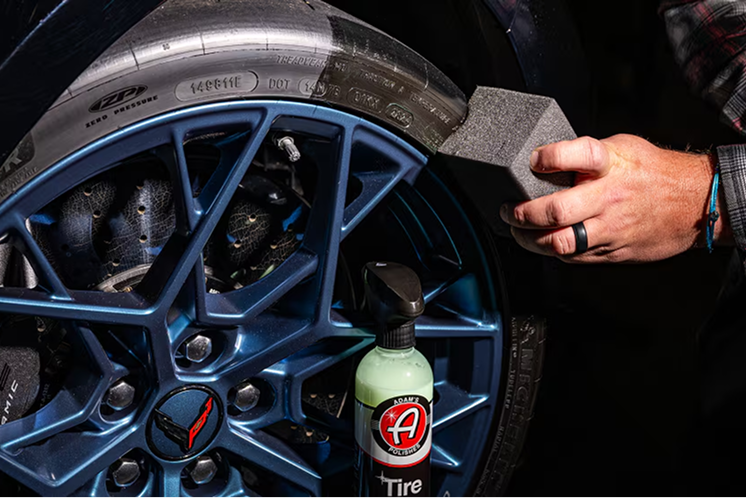 Close-up of one of a Corvette’s multi-spoke forged wheels with tire dressing being applied by hand.