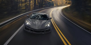 Front View of a 2025 Gray Chevy Corvette E-Ray Driving Down the Road with Its Headlight on
