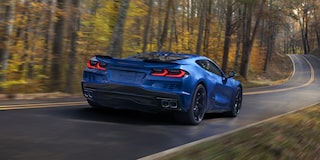 Three Quarters Rear View of a Blue Chevy Corvette E-Ray Driving Down the Road Surrounded by Trees