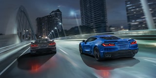 Two 2025 Chevy Corvette E-Ray Racing Down the Road under a Night Sky in a City