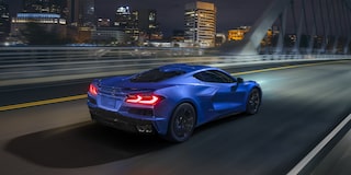 Three Quarters Rear View of a 2025 Blue Chevy Corvette E-Ray Driving Down the Road Under a Night Sky