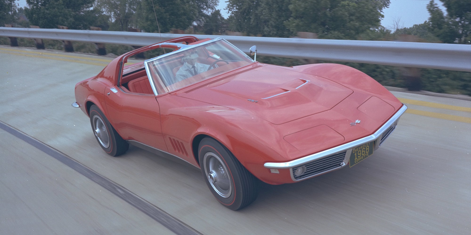 Dreiviertelansicht eines scharlachroten Corvette C3 Cabriolets mit durchdrehenden Reifen auf einer Autobahn.