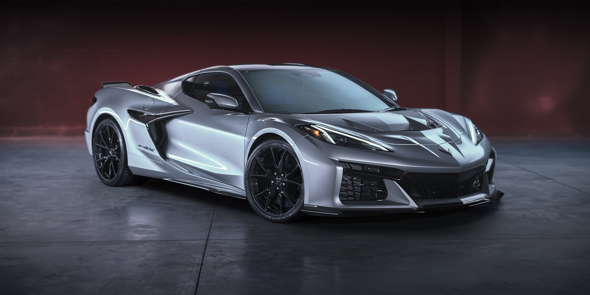 Dreiviertelansicht einer Chevrolet Corvette ZR1X (2026) in Blade Silver Metallic, auf polierten schwarzen Platten geparkt.