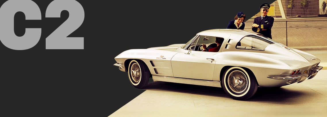 Three-quarter rear view of a silver Corvette C2 coupé, parked outside with airline crew talking to the driver.  