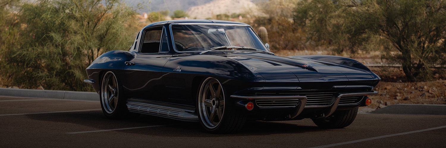Three-quarter view of a dark-blue classic Corvette, parked on a desert road.