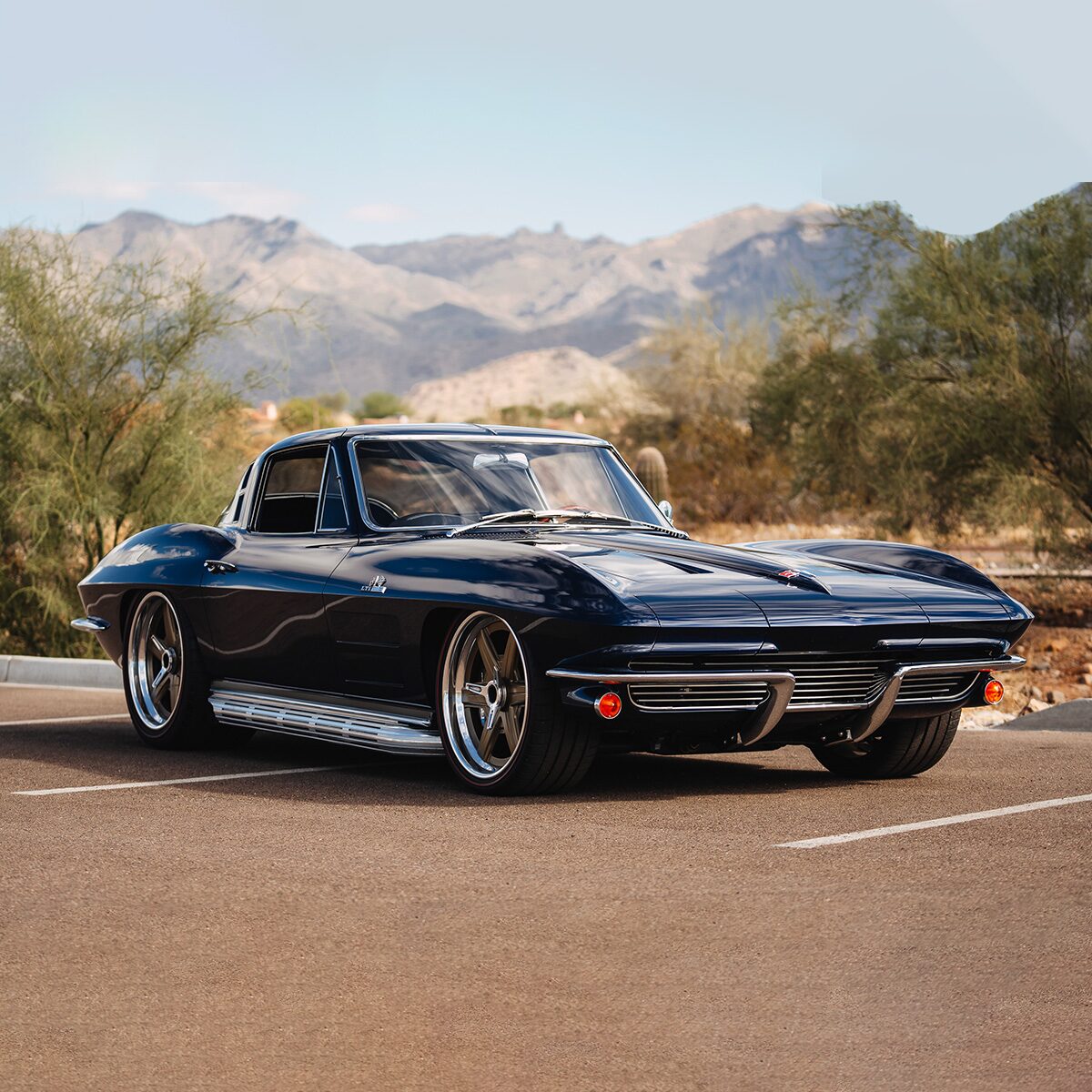 Three-quarter view of a dark-blue classic Corvette, parked on a desert road.