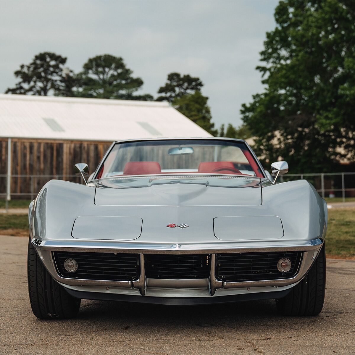 Front view of a silver classic Corvette with pop-up headlights and chrome accents, parked outdoors.