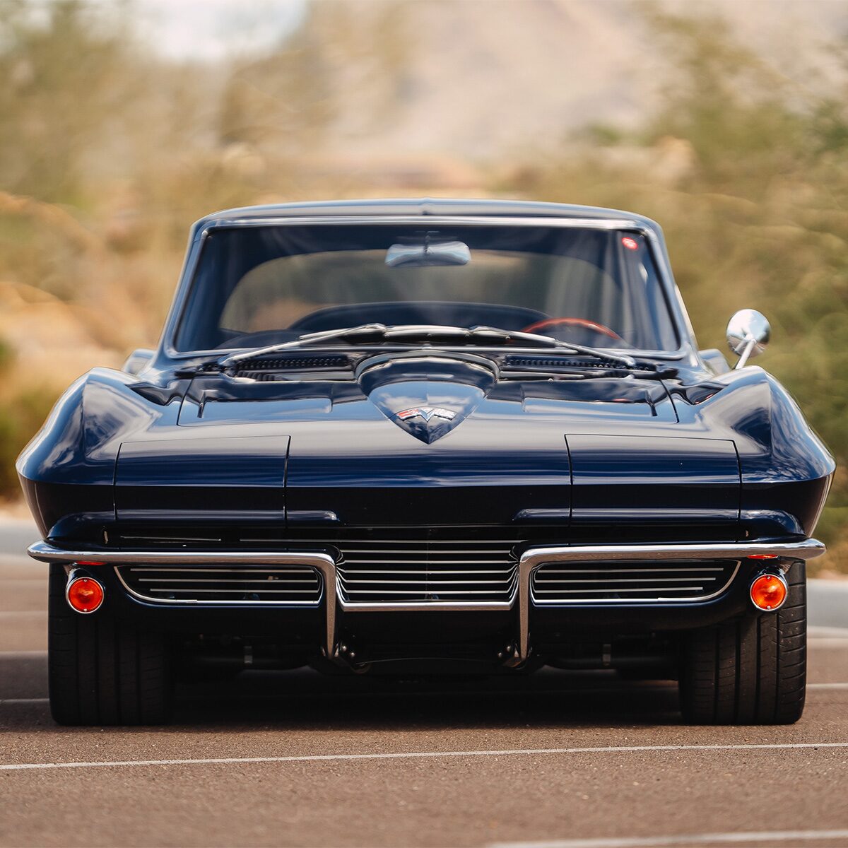 Front view of a dark-blue 1964 Corvette Stingray with split front bumper and chrome details, parked outdoors.