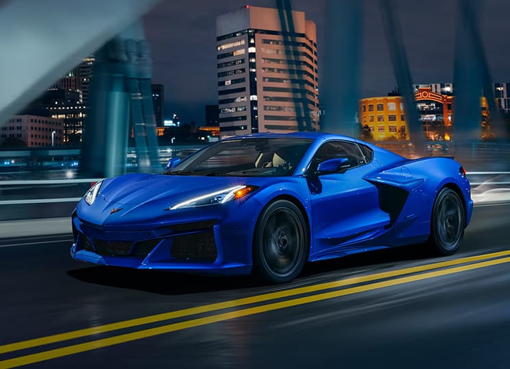 Three-quarter view of Corvette E-Ray in Riptide Blue Metallic on a city motorway at night.