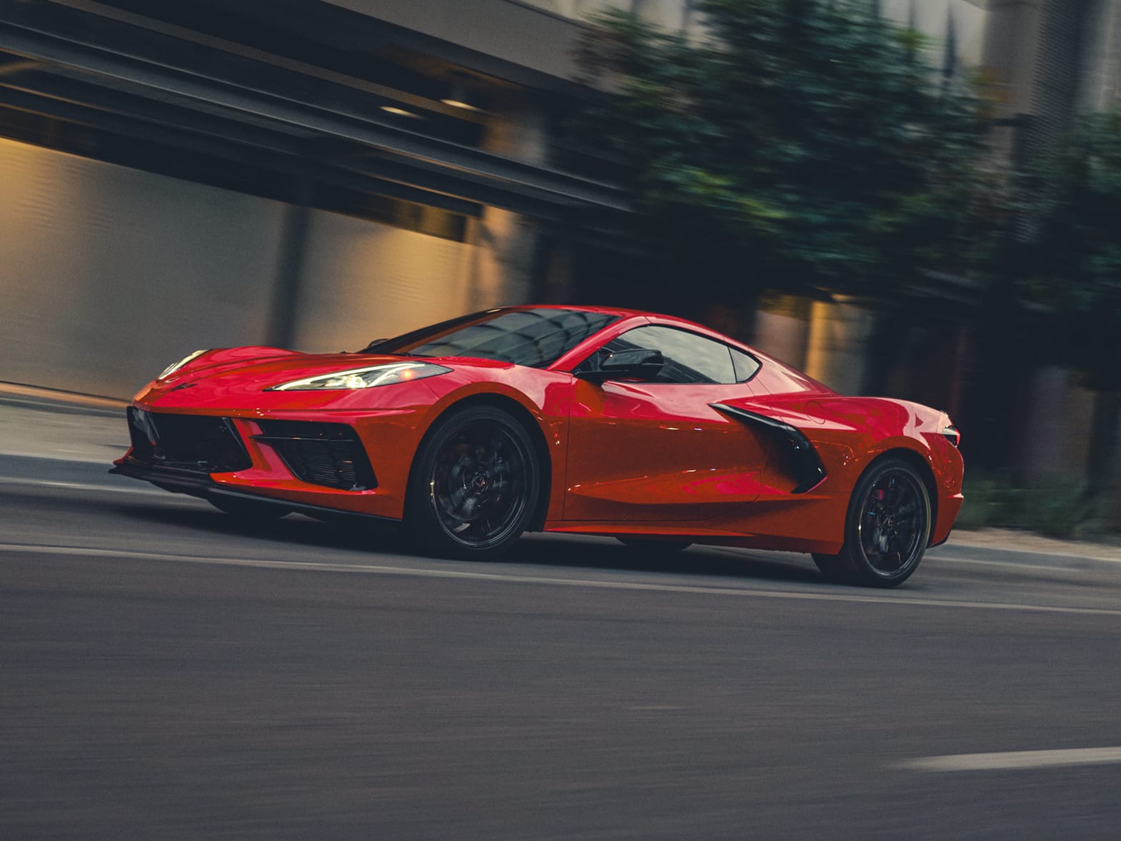 Three-quarter view of a Corvette Stingray coupé in Torch Red cruising a city highway.