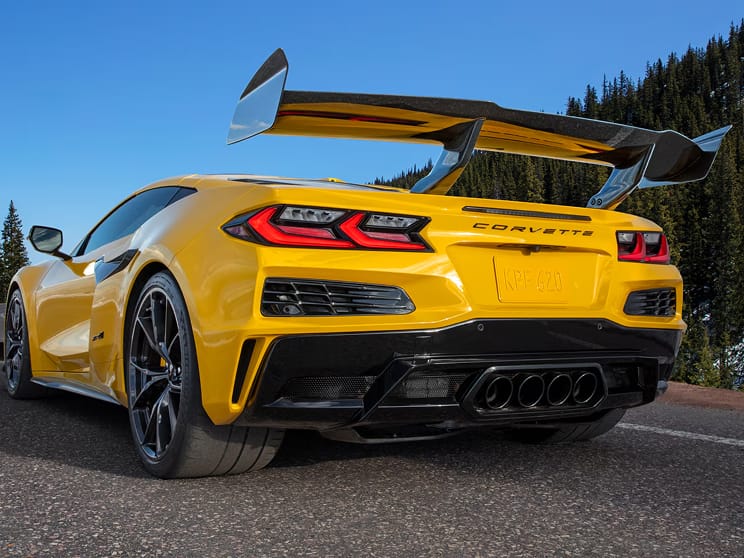Three-quarter rear view of a Chevy Corvette ZR1 hypercar, finished in Competition Yellow Tintcoat Metallic. Parked on a racetrack, with one gull-wing door open.