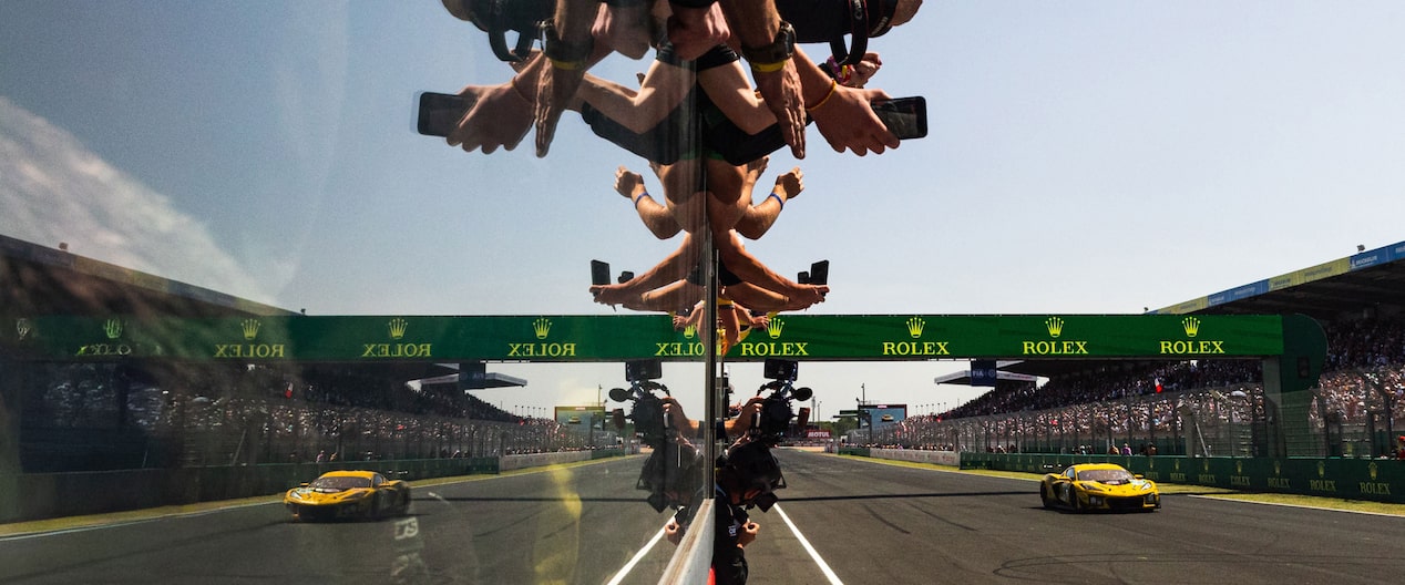 Mirrored glass reflects the cameras in hands of photographers, as they capture the No. 33 Chevrolet Corvette burning rubber at grandstand-lined Le Mans. 
