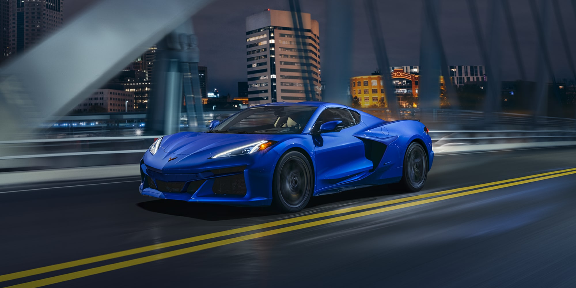 Three Quarters View of a 2025 Blue Chevy Corvette Driving Down the Bridge at Night
