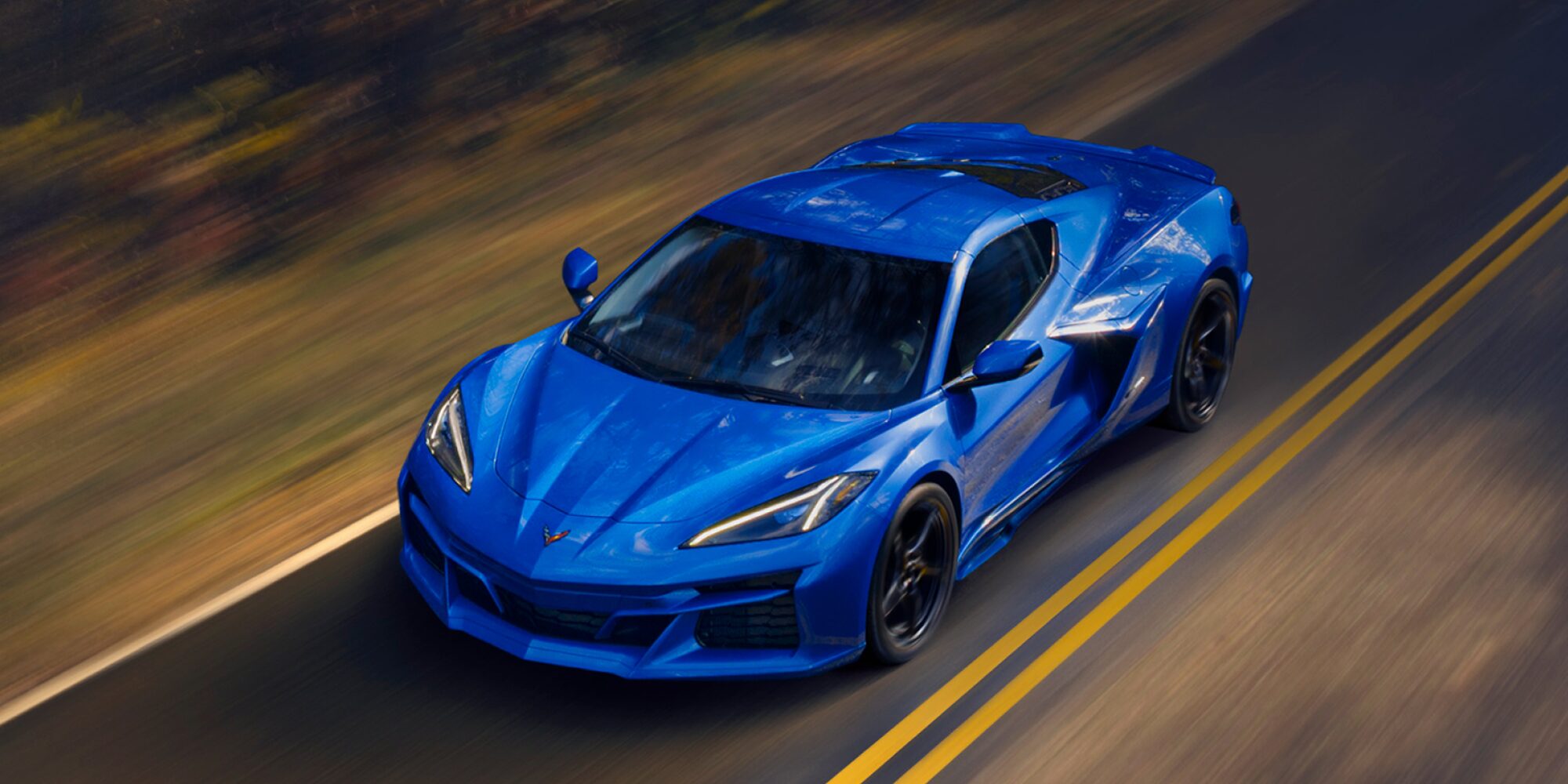 Front View of a 2025 Blue and Gray Chevy Corvette E-Ray Racing Down the Road on a Bridge